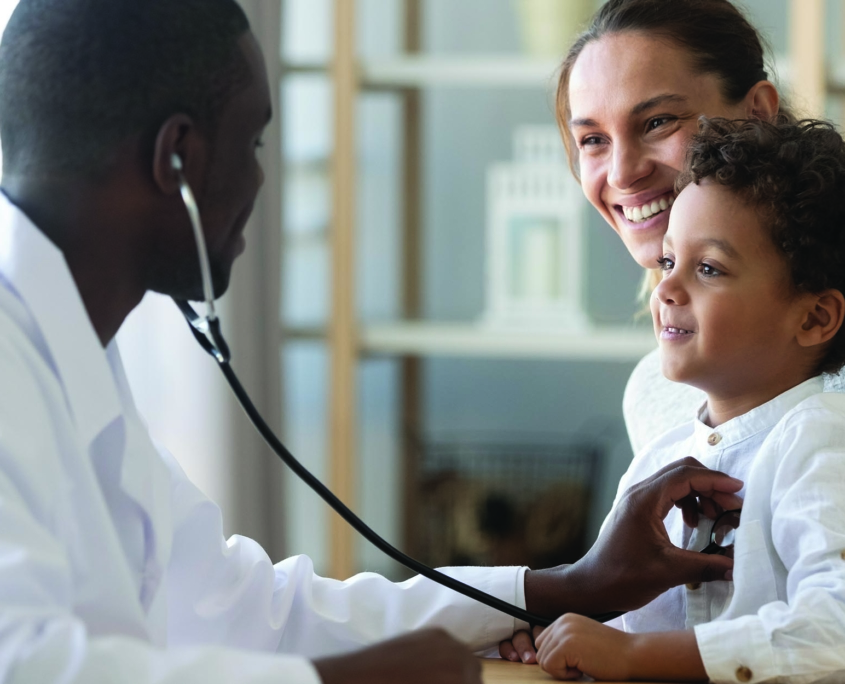 Smiling mother holding her young son while a doctor listens to his heart with a stethoscope