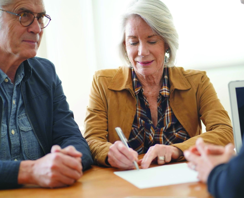 Smiling older couple signing retirement plan papers with an insurance agent