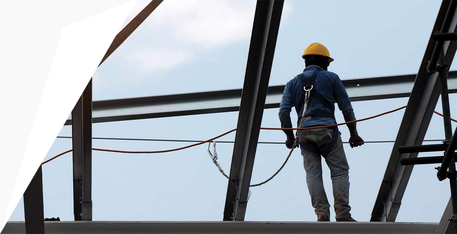 Construction worker in harness and hard hat standing on top of metal beams