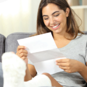 Smiling woman with leg cast reading a letter on a couch