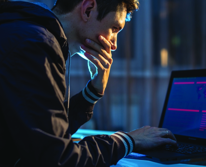 Hacker in dark room hunched over a laptop