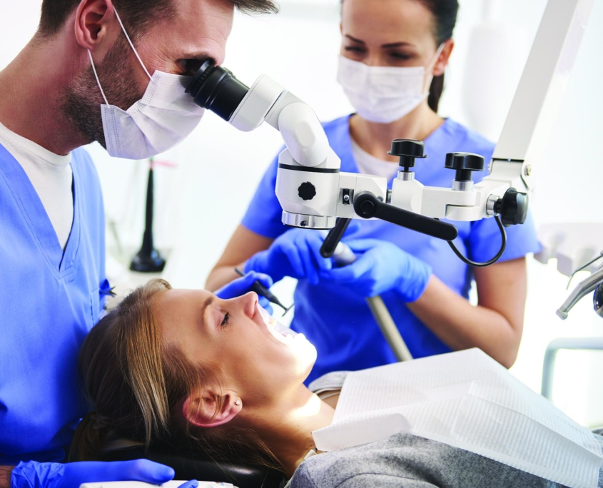 Oral surgeon viewing a patient's teeth through a scope while an assistant prepares for a procedure