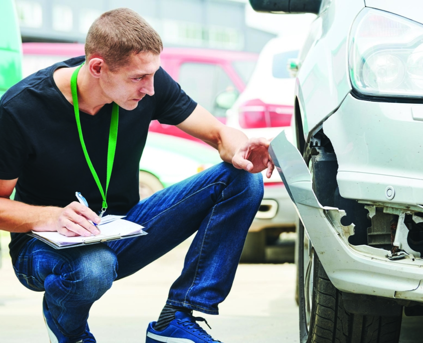 Auto insurance adjustor kneeling to assess damage on front of silver car