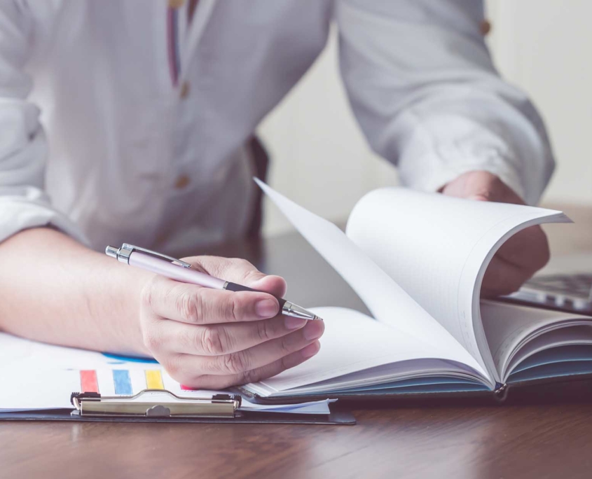 close up view of man behind desk flipping through pages in notebook