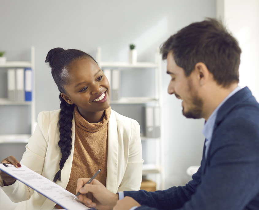 smiling woman in office setting holds up form while man signs it