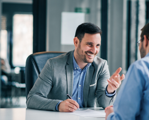 smiling man behind desk fills out a form while speaking to client