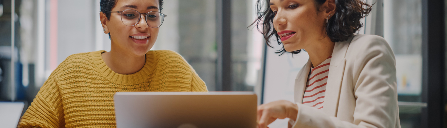 two women sitting behind a desk look at computer screen