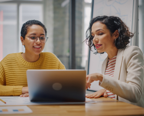 two women sitting behind a desk look at computer screen