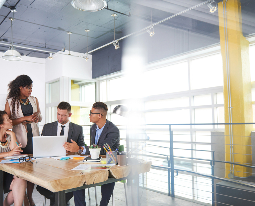 Four coworkers chatting at a table in industrial office setting