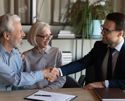 Shaking hands. Smiling young man real estate broker handshaking with older family couple after buying selling property_